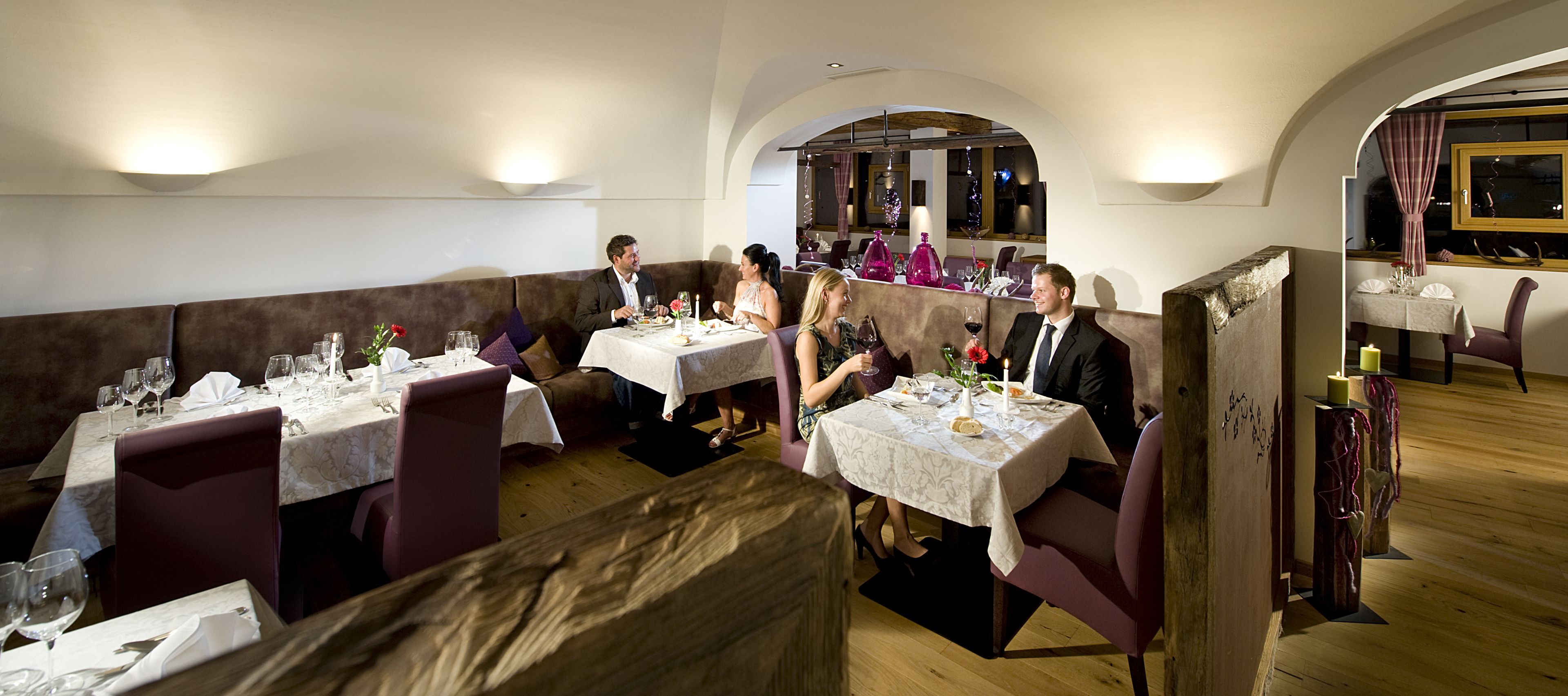 A restaurant with multiple tables and booths, each set with wine glasses, plates, and cutlery.