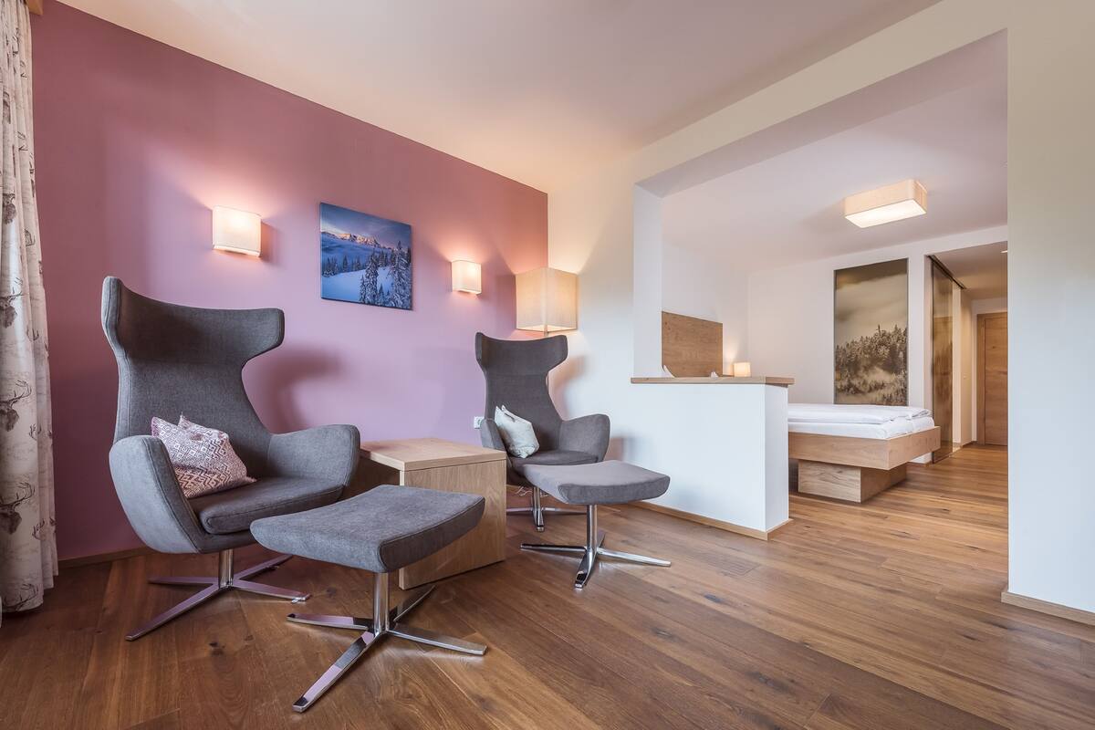 A modern room with two grey armchairs, a wooden desk, and a bed.
