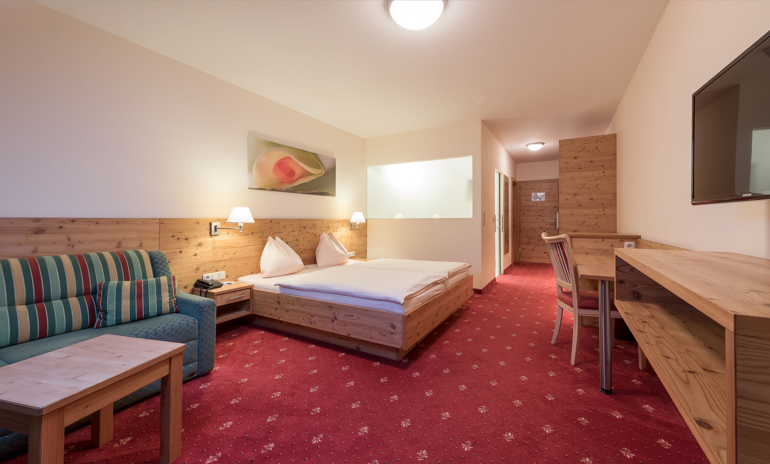A hotel room with a bed, a sofa, a desk, and a TV.