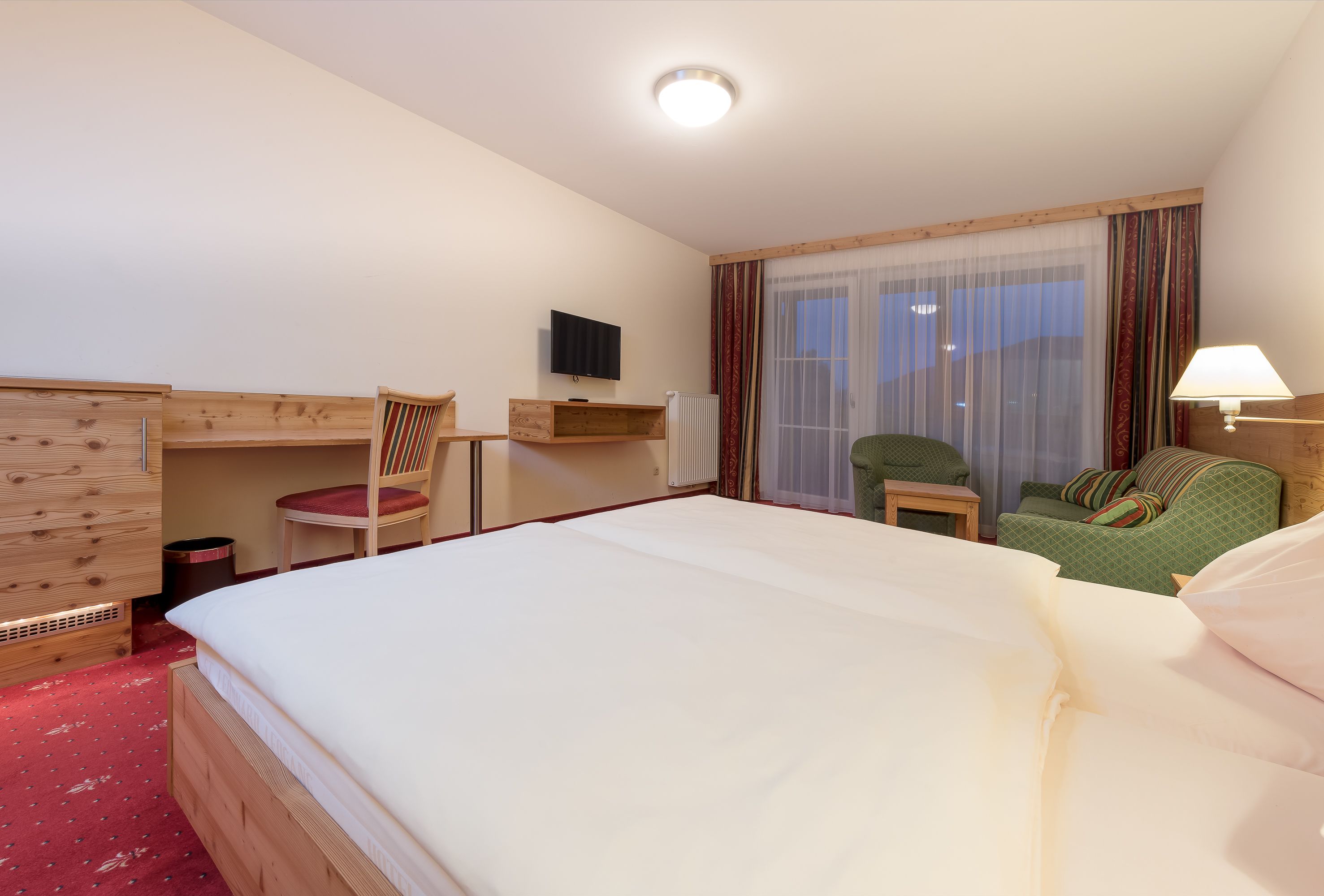 Een hotelkamer met een groot bed, een houten dressoir, een bureau, een stoel, een televisie en een raam met gordijnen.