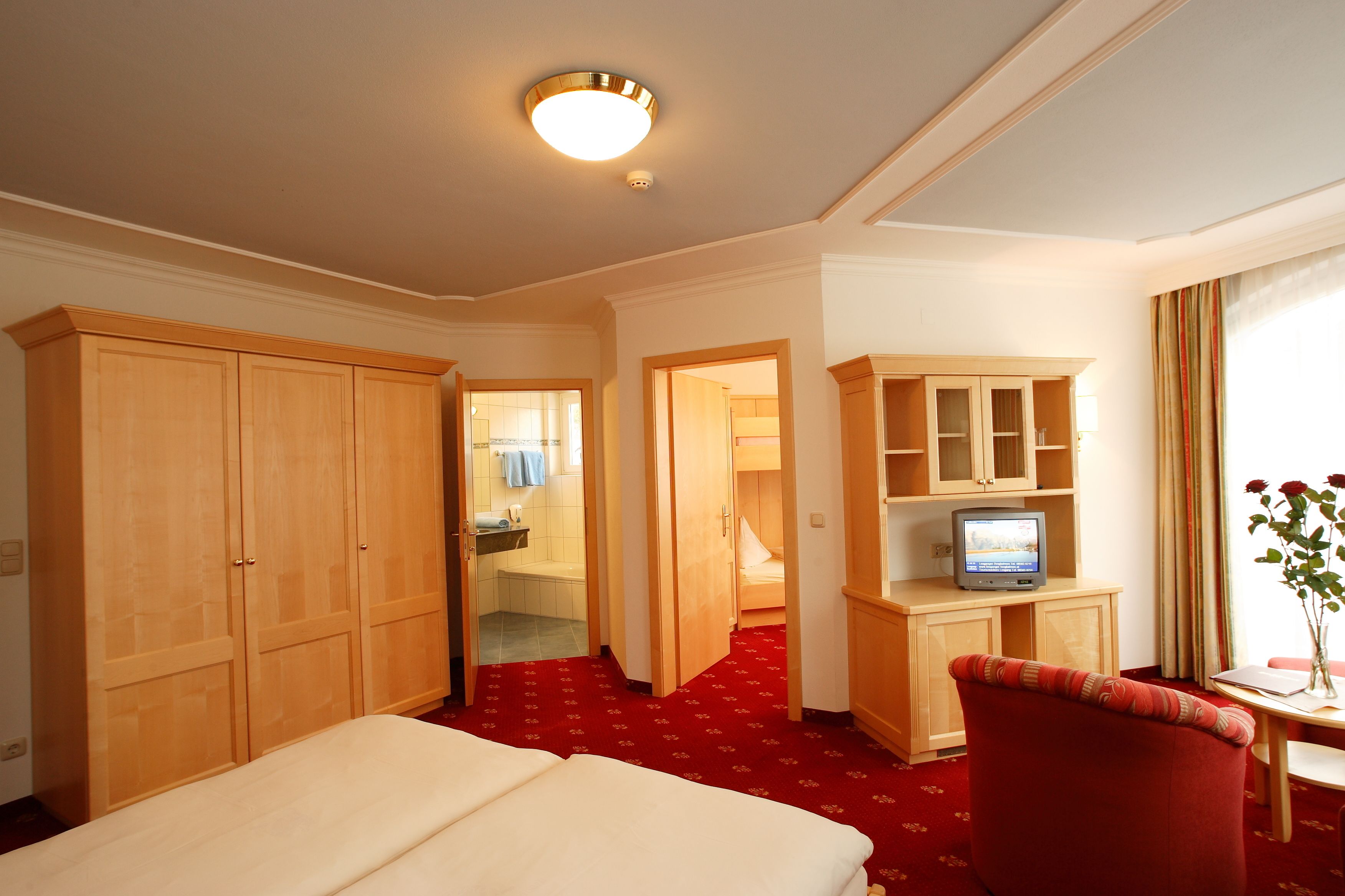 A hotel room with a bed, a red carpet, a TV, a desk, and a chair.