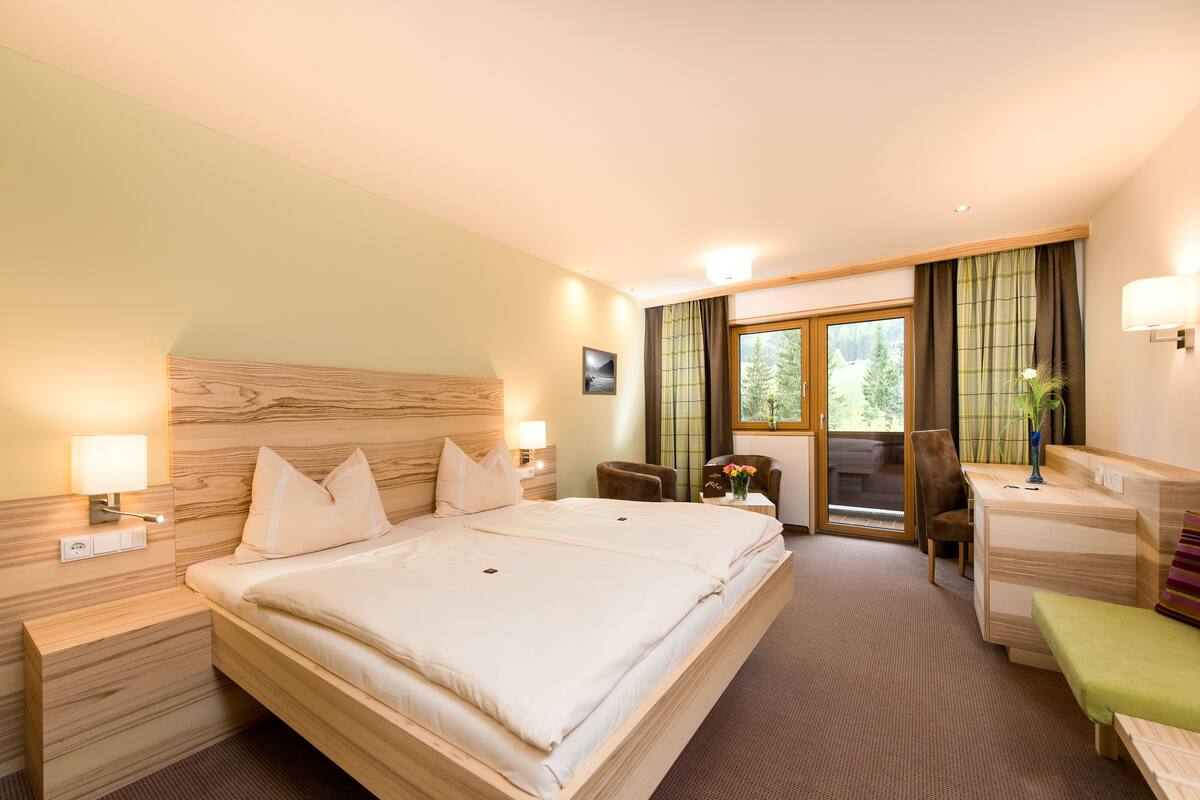 A hotel room with a large bed, a desk, a chair, and a view of the outdoors.