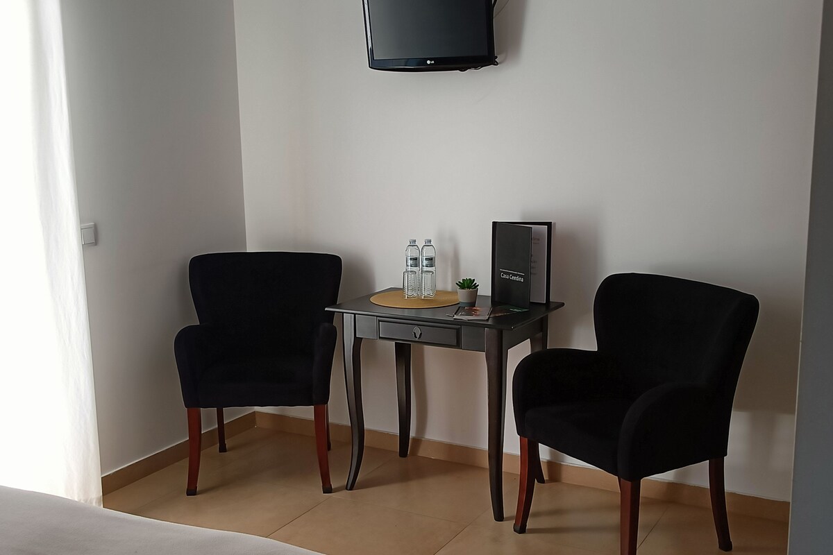 A small, modern room with two black chairs, a small table with a water bottle, a plant, and a black sign.