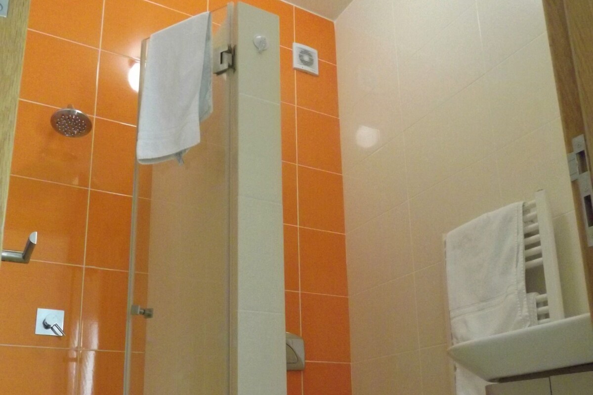 A bathroom with orange tiles, a glass shower enclosure, a toilet, and a sink with a towel hanging on the wall.