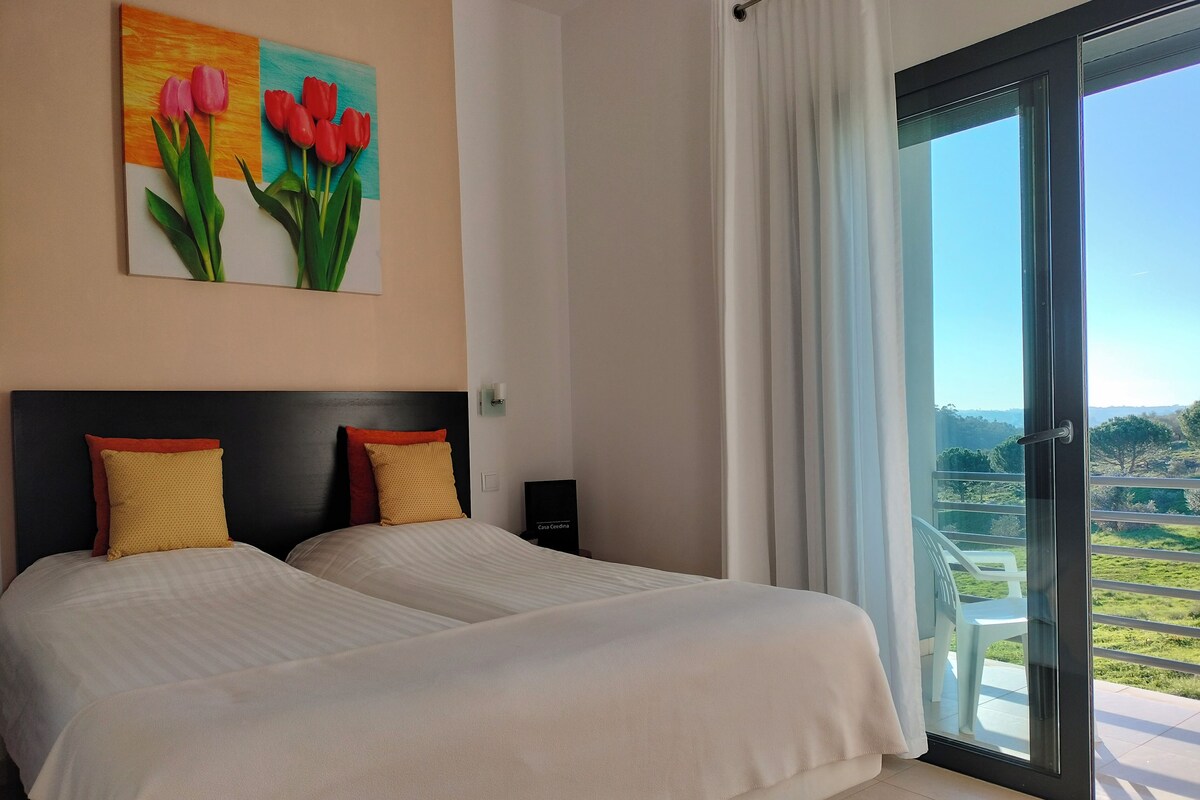 A double bed with two pillows, a painting of tulips, a nightstand, and a sliding glass door to a balcony.