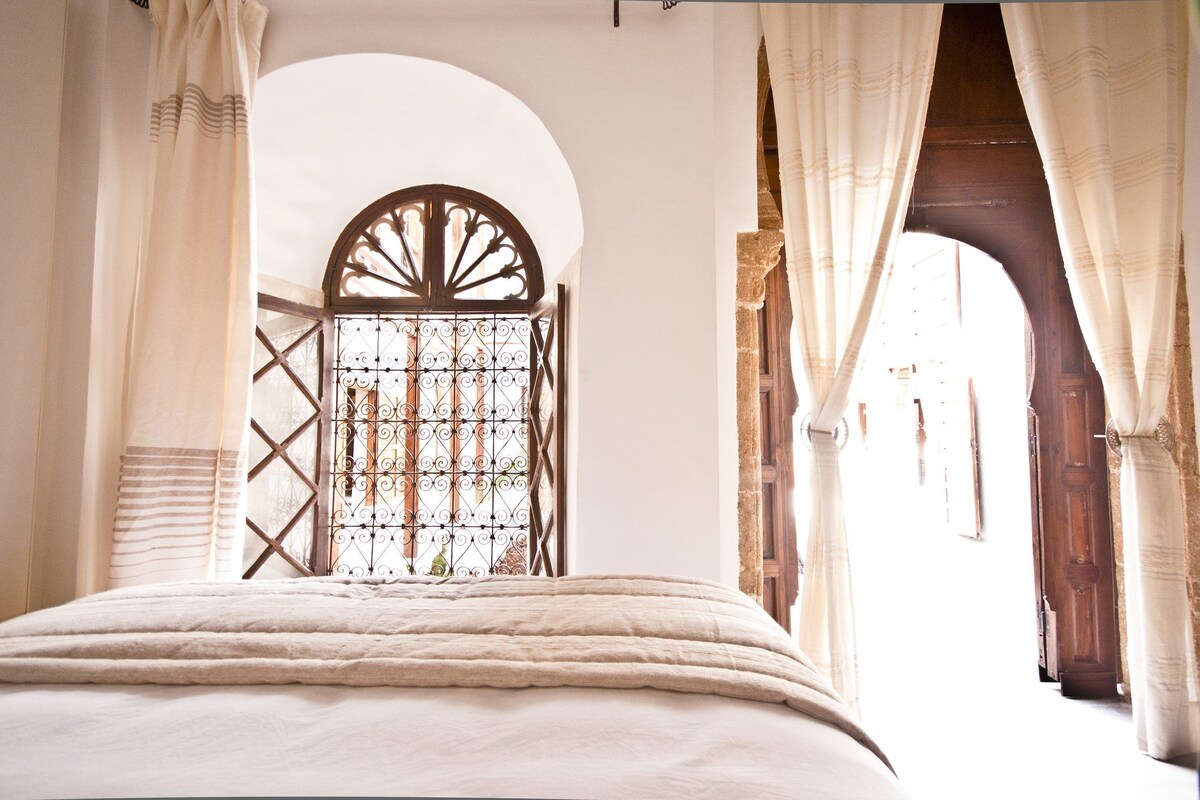 Une chambre à coucher avec un grand lit, une fenêtre en arc de cercle et des rideaux.