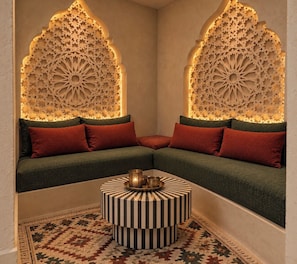 Un rincón amoblado con un sofá, almohadones, un tapete estampado y una pared decorativa con diseños intrincados.