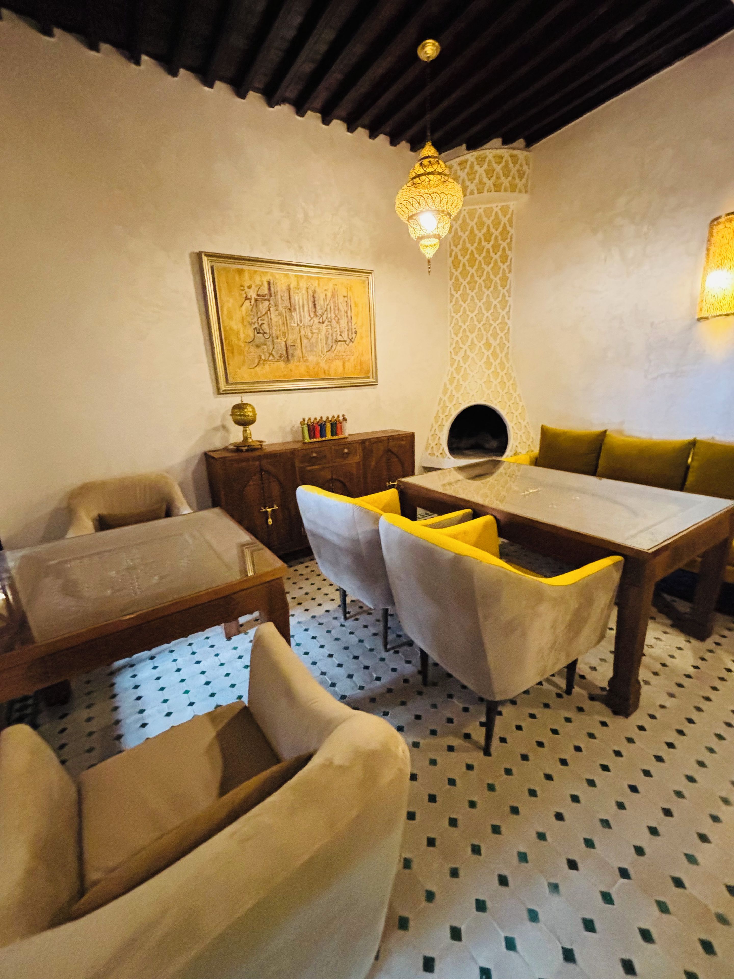 A dining area with a table, chairs, and a sofa. There is a wall-mounted artwork and a patterned wall.