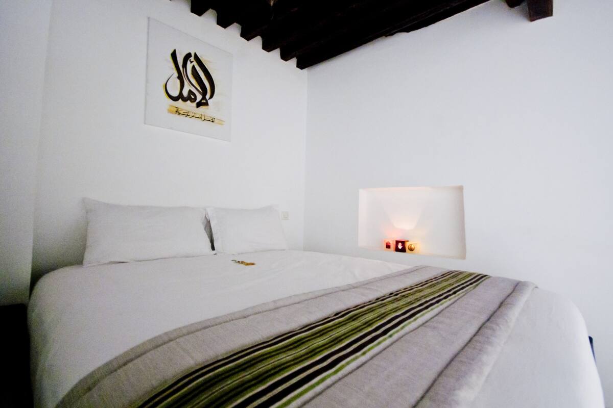 A neatly made bed with a striped blanket, a wall-mounted artwork, and a bedside table with a lamp.