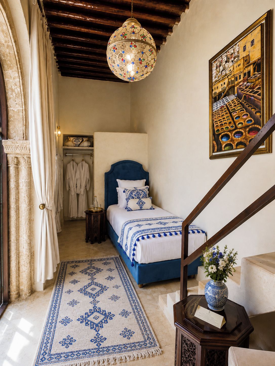 A bedroom with a bed, a hanging light fixture, a painting, and a staircase.