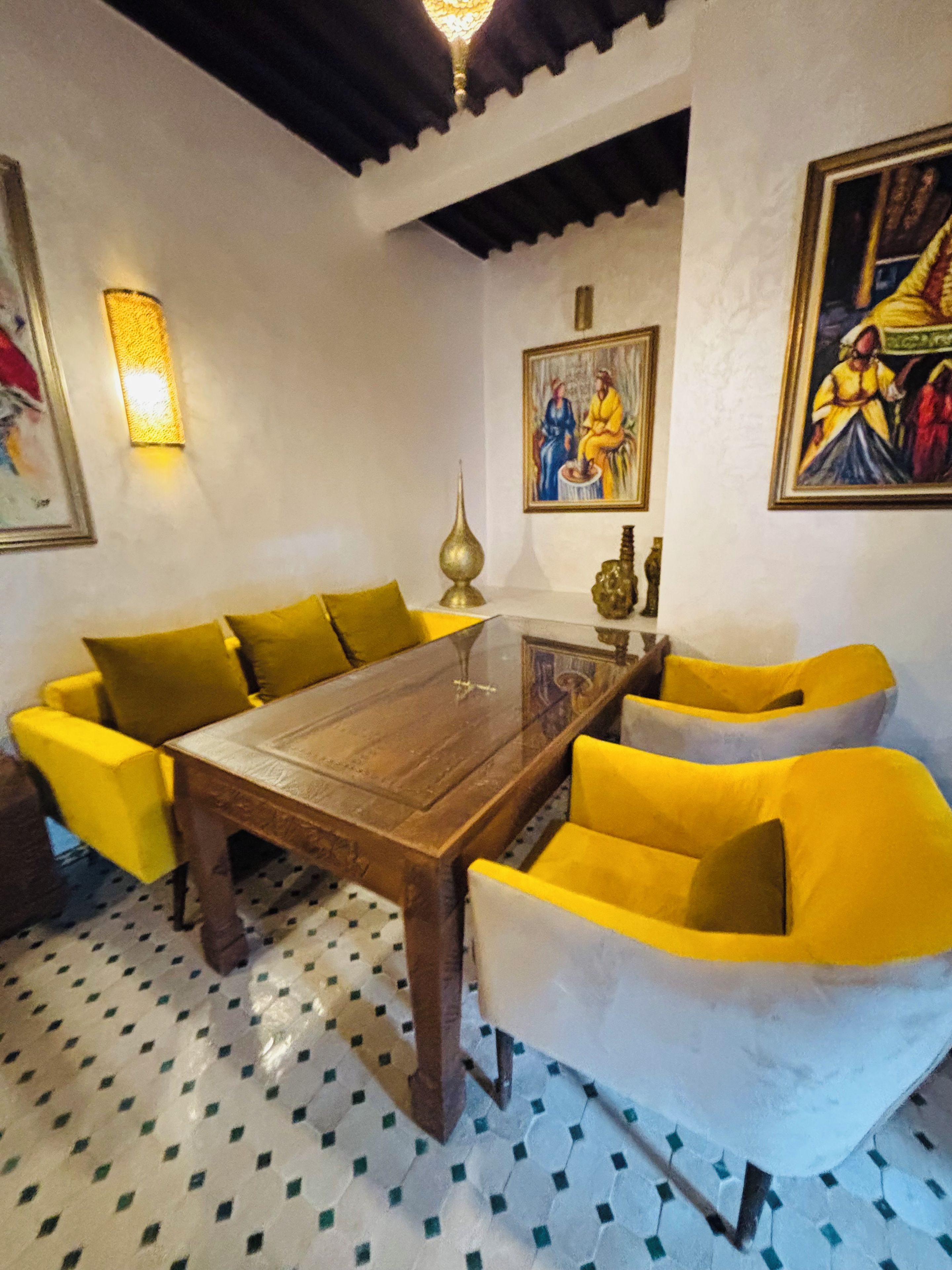 A dining area with a wooden table surrounded by yellow chairs, a patterned floor, and wall-mounted artwork.