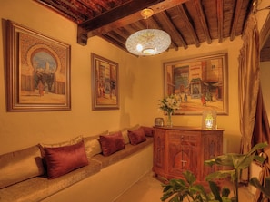 Una habitación con techo de madera, un sofá con cojines, un armario y cuadros enmarcados en la pared.
