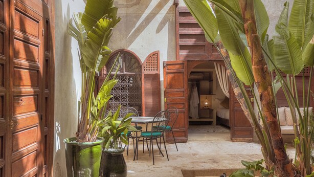 Un pati amb portes de fusta, una taula, cadires i plantes en testos.