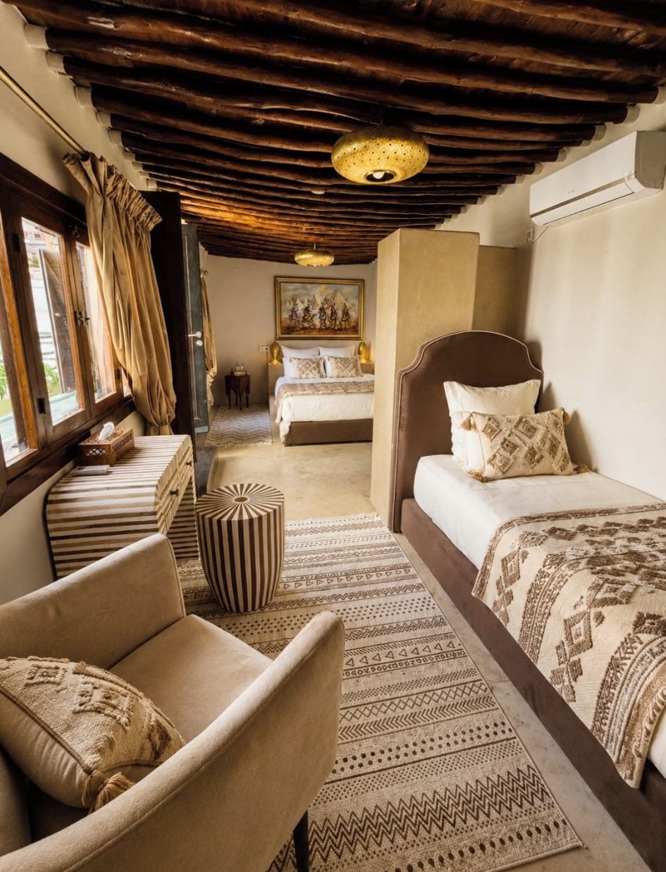 A hotel room with a wooden ceiling, a bed with patterned bedding, a sofa with cushions, a small table, and a rug.