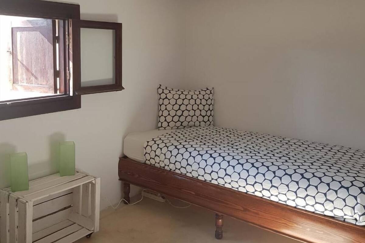 A bedroom with a bed, a nightstand, a mirror, and a window.