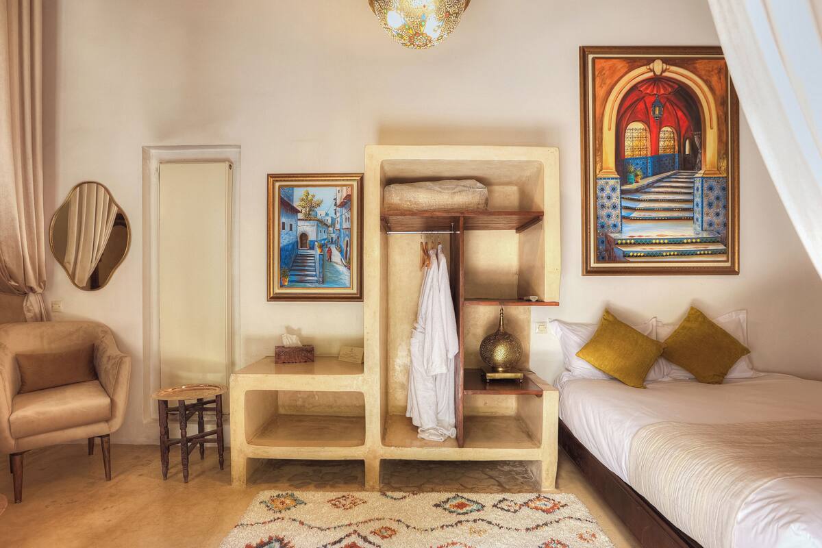A bedroom with a bed, a wooden chest of drawers, a mirror, a painting, and a patterned rug.
