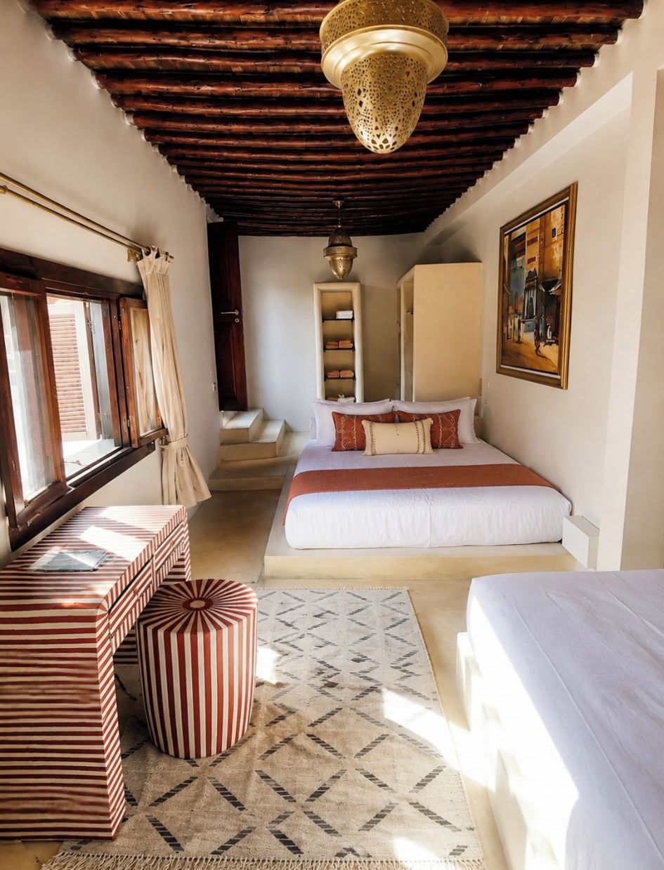 A bedroom with a bed, a window, a wardrobe, a painting, and a hanging light fixture.