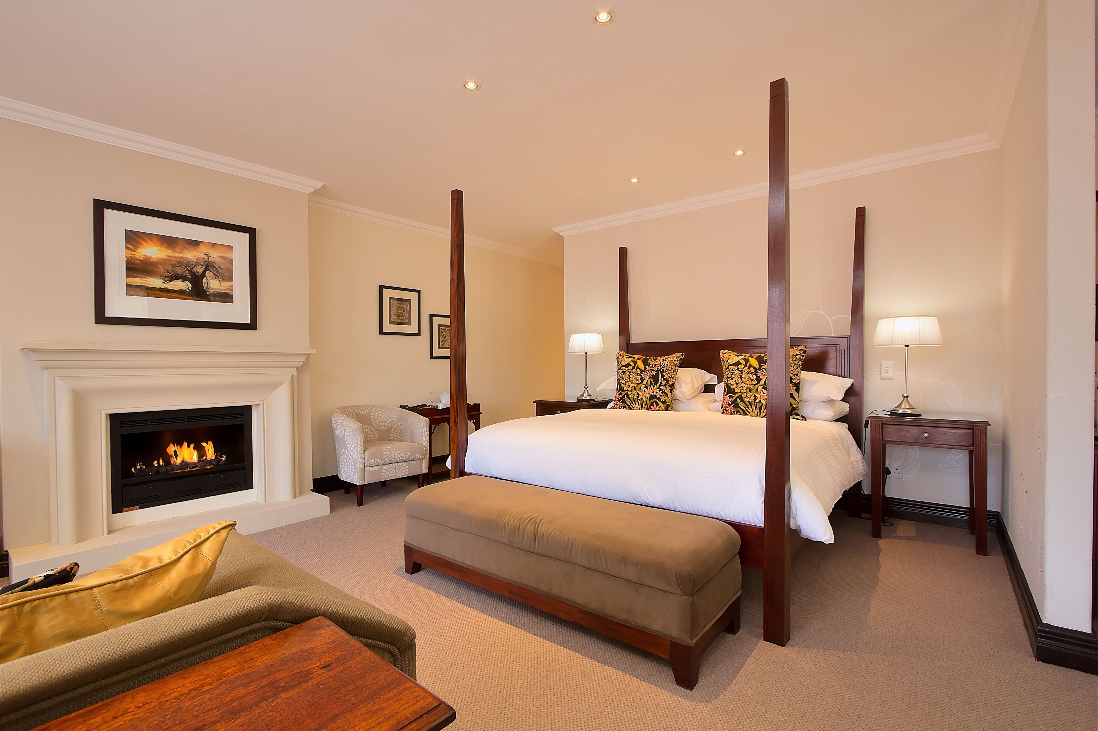 A spacious bedroom with a large bed, a fireplace, and a view of the sunset.