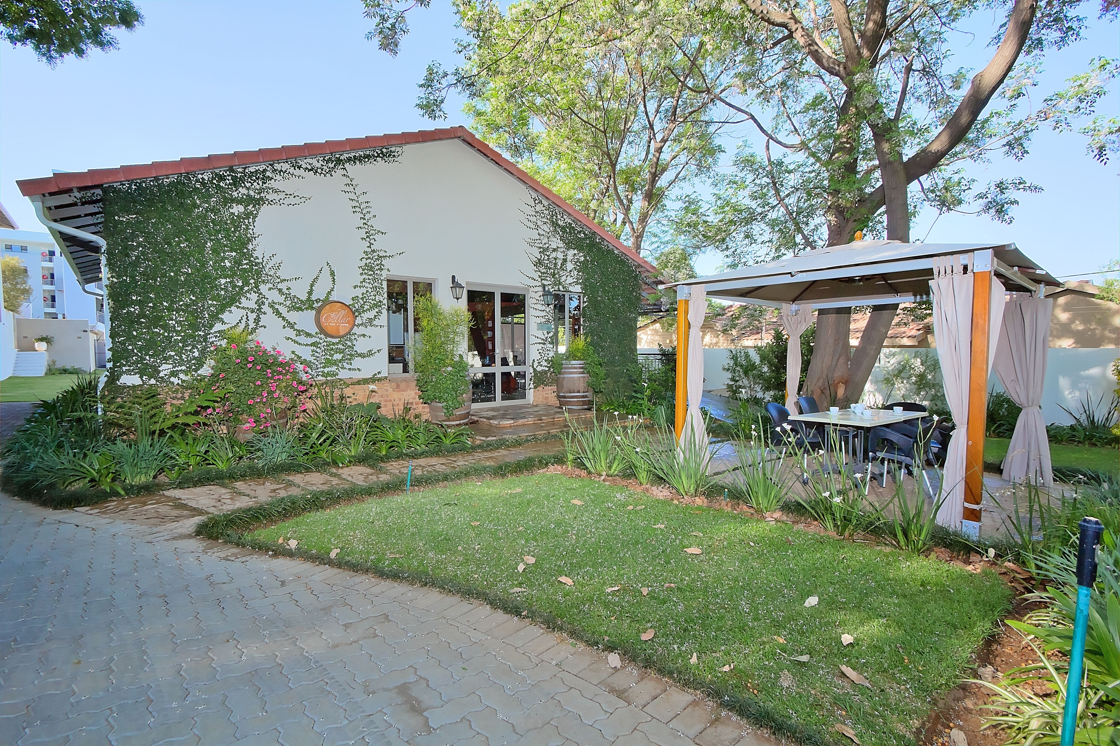 A house with a garden, a patio with a table and chairs, and a pergola.