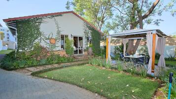 A house with a garden, a patio with a table and chairs, and a pergola.