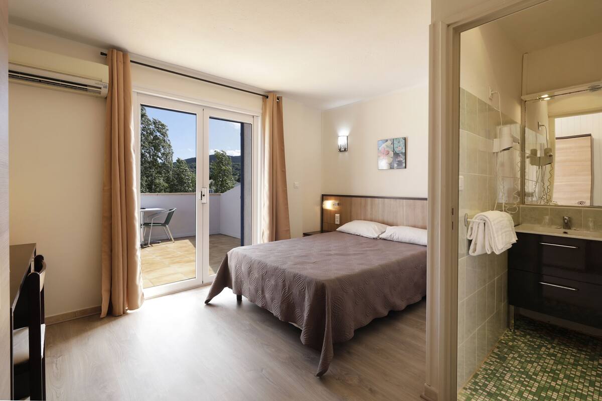 A bedroom with a bed, a bathroom with a shower, and a balcony with a chair.
