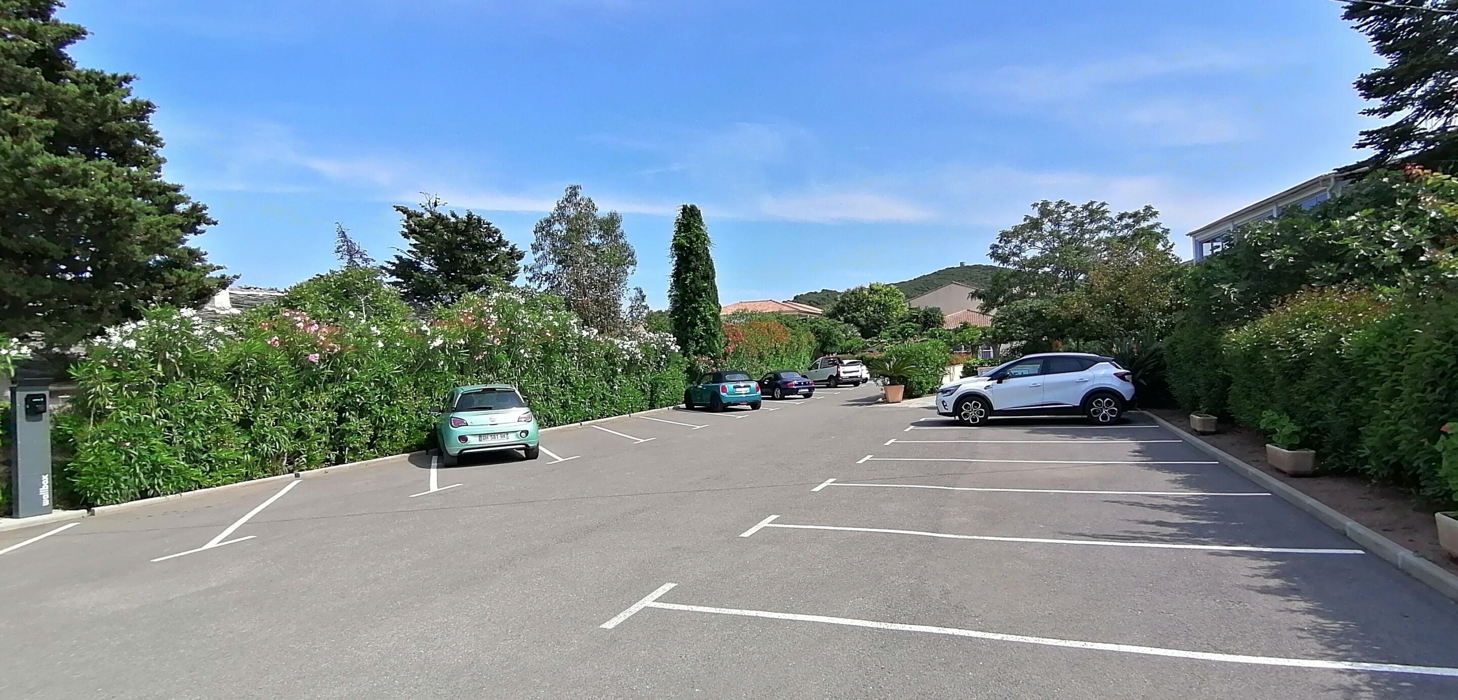 A parking lot with several cars parked, surrounded by greenery and buildings.