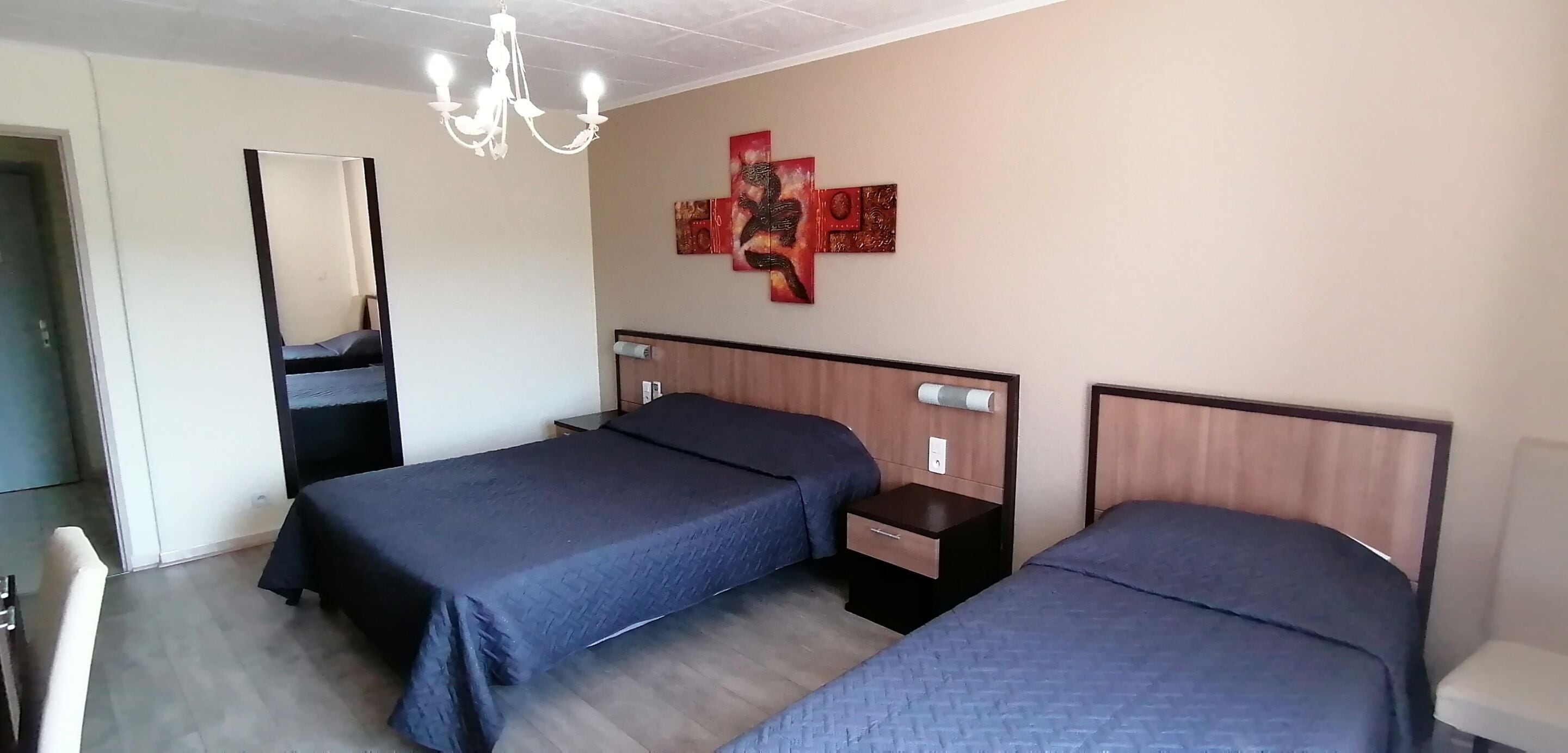 Een hotelkamer met twee bedden, een spiegel, een kroonluchter en kunst aan de muur.