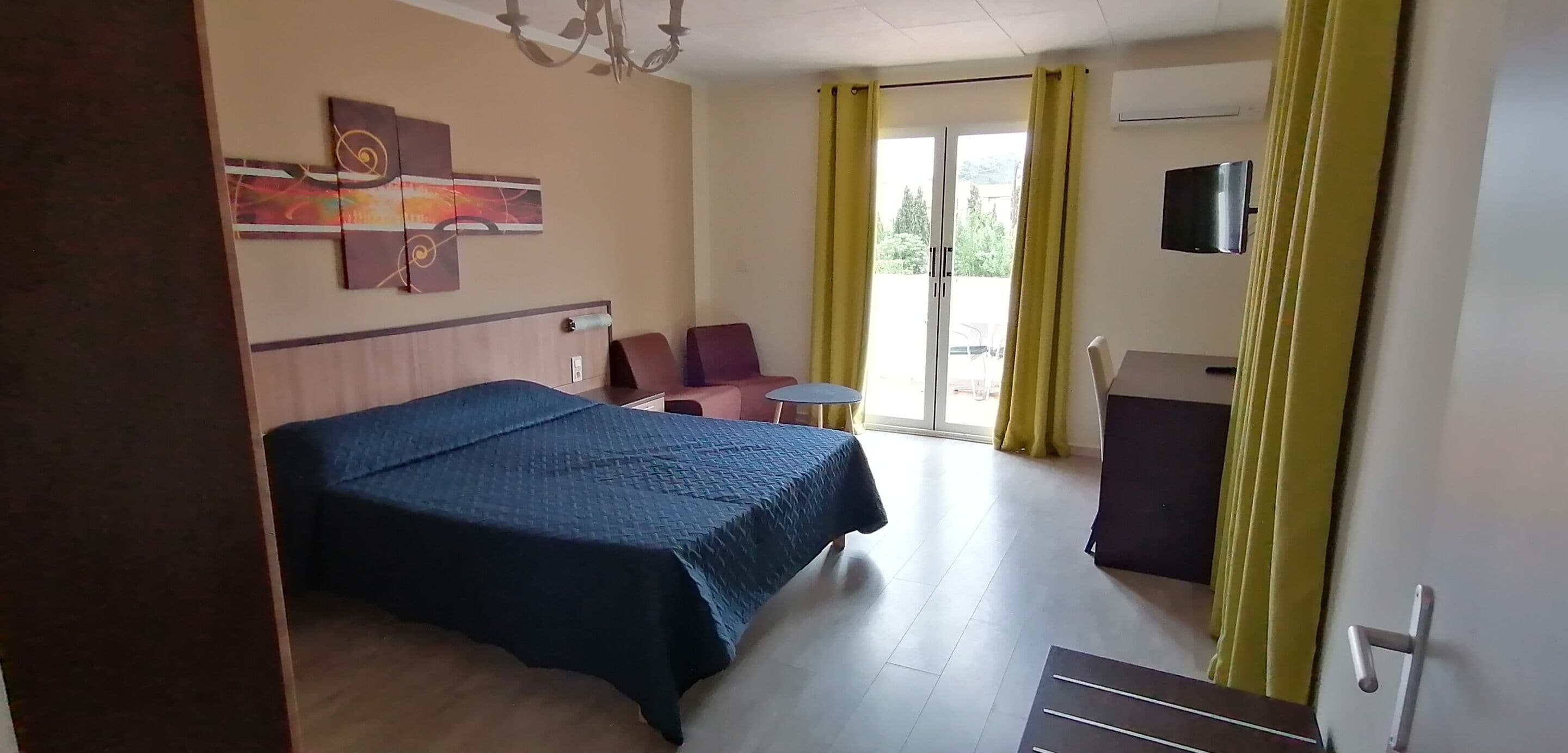 A hotel room with a bed, a desk, a chair, a TV, and a window with curtains.