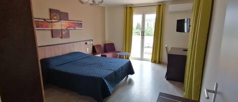 A hotel room with a bed, a desk, a chair, a TV, and a window with curtains.