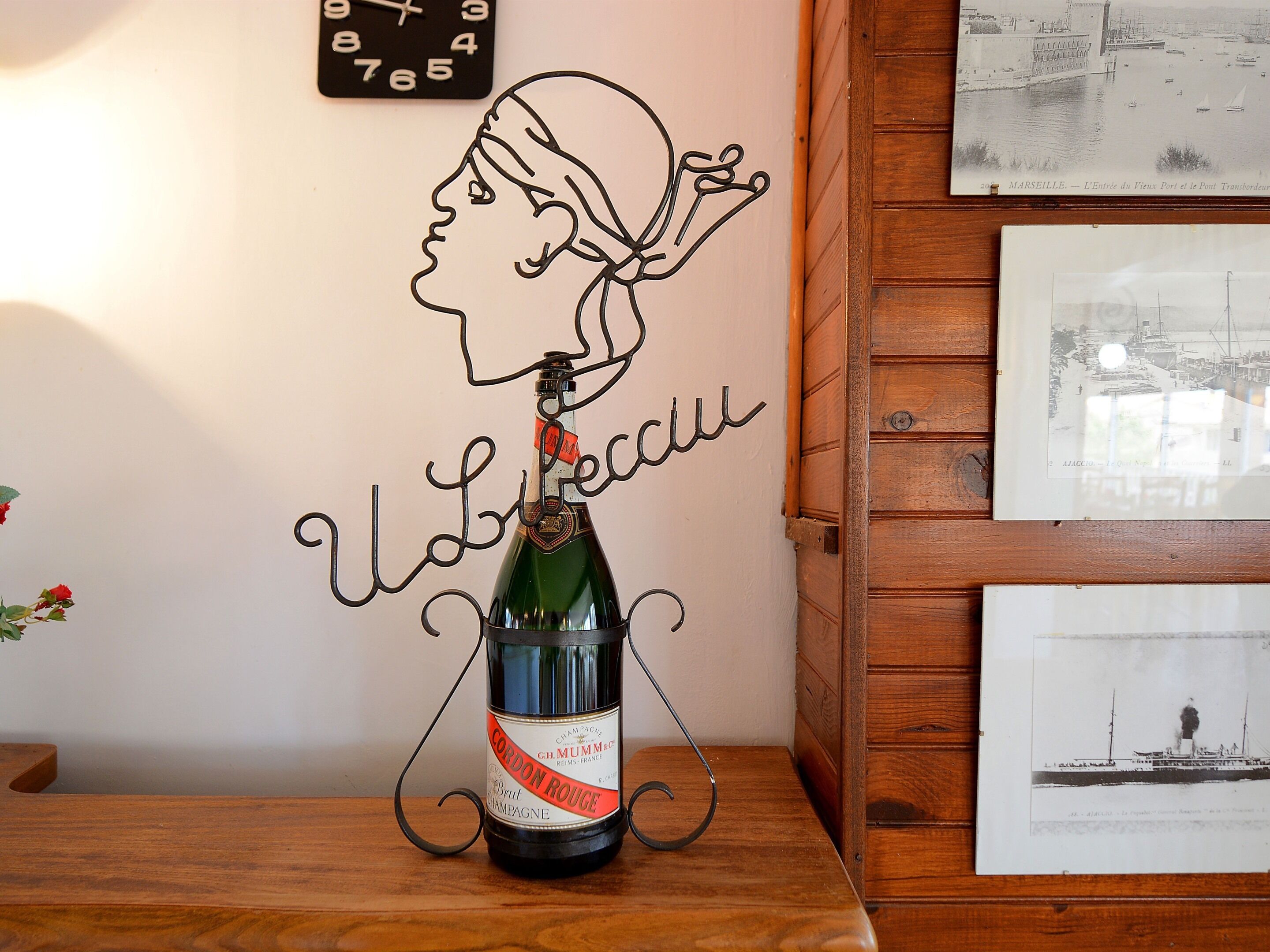 Une bouteille de champagne posée sur un présentoir en métal, une horloge murale et des photos encadrées sur une table en bois.