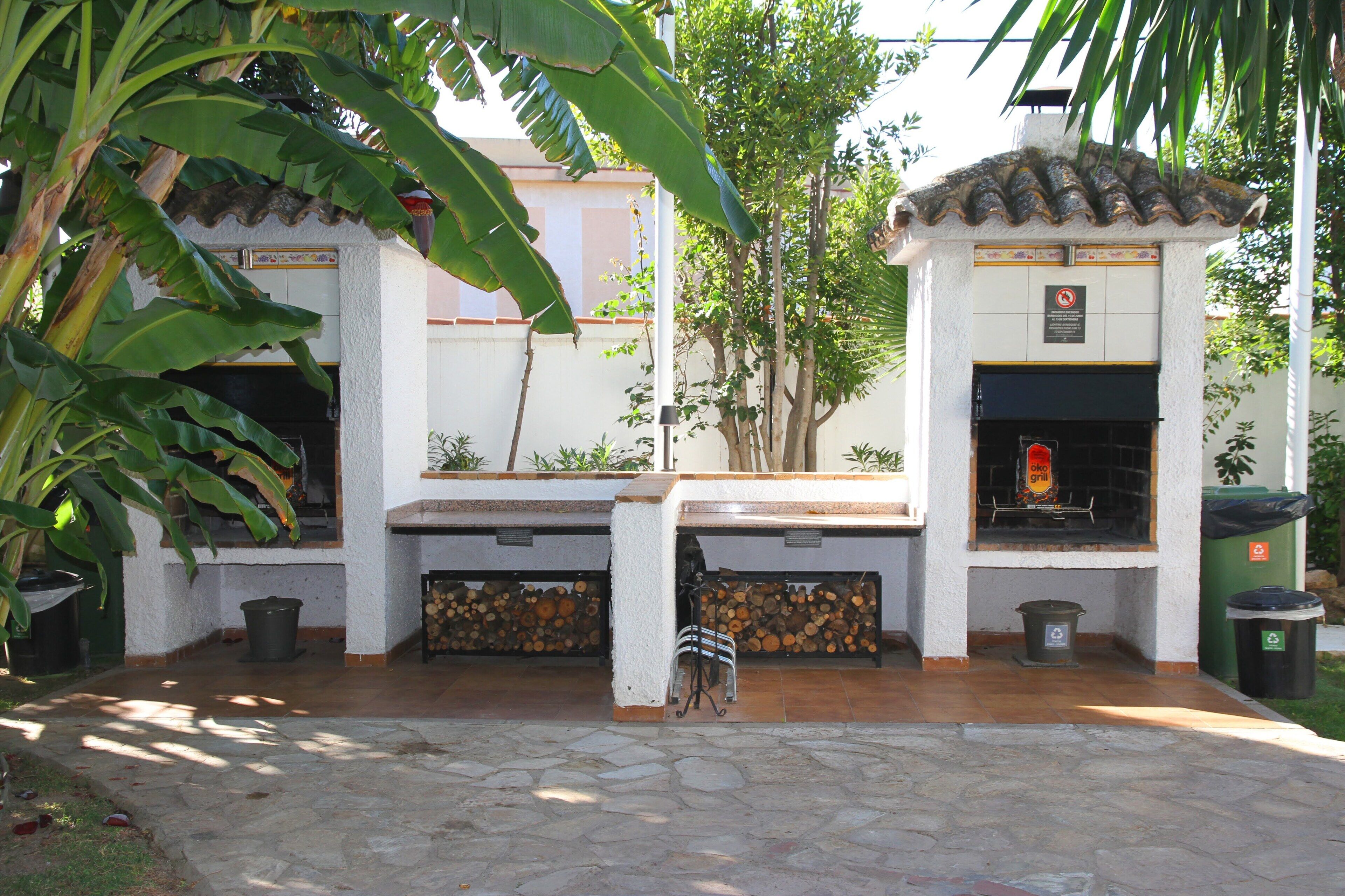 An outdoor patio with a barbecue grill, a stone floor, and a white wall with a tiled roof.