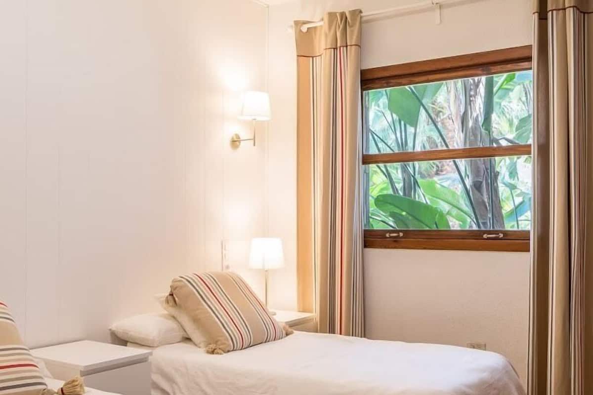 A hotel room with two beds, a window with curtains, and wall-mounted lamps.