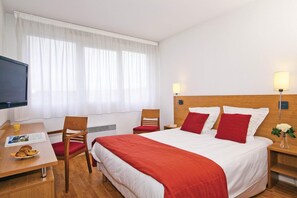 A hotel room with a bed, a desk, a chair, a TV, and a window with curtains. - Séjours & Affaires Lyon Saint-Nicolas (Lyon)