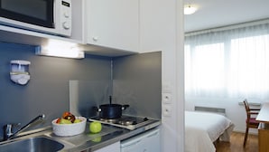 A compact kitchenette with a microwave, stove, sink, and a bowl of fruit. - Séjours & Affaires Lyon Saint-Nicolas (Lyon)