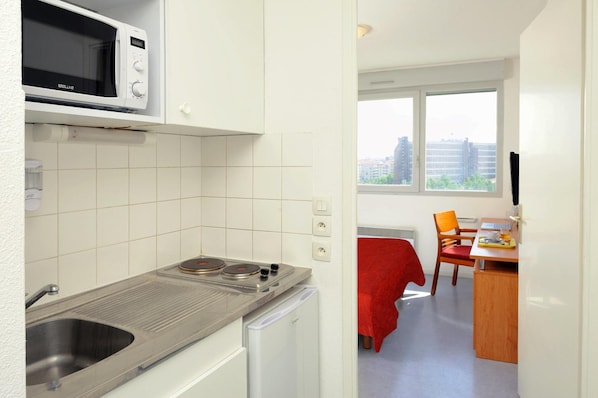 A compact kitchen with a microwave, sink, and stove, leading to a dining area with a red table and chairs.