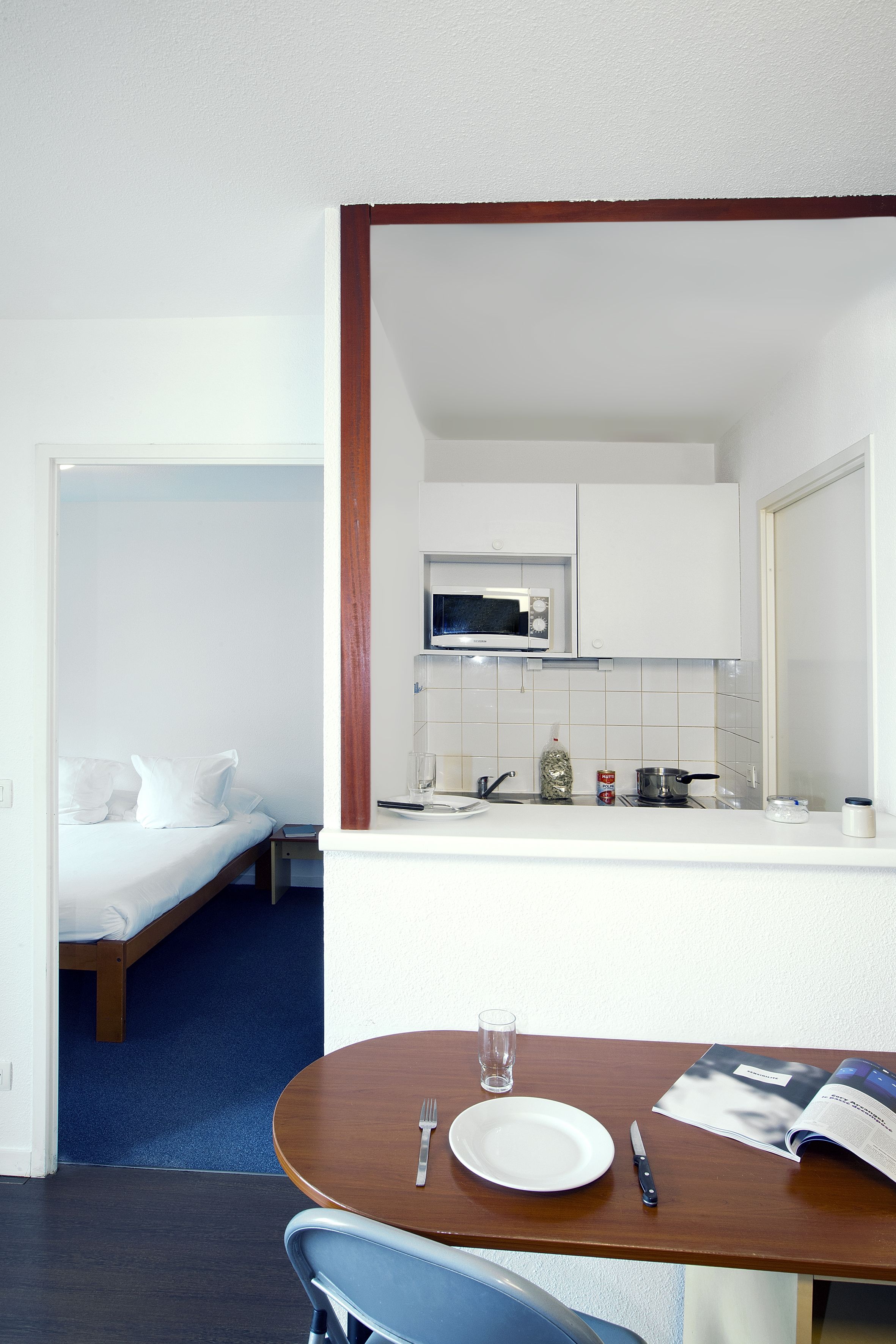 Ein kompaktes Hotelzimmer mit einem Bett, einer kleinen Küchenzeile und einer Essecke mit Tisch und Stühlen.
