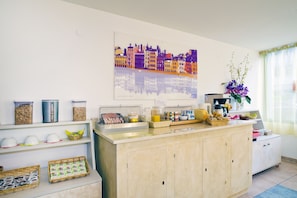 A kitchen with a countertop, shelves with food items, a coffee machine, and a decorative wall piece.