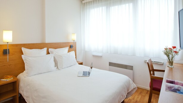 A hotel room with a large bed, a desk with a laptop, a chair, and a window with sheer curtains. - Séjours & Affaires Lyon Saint-Nicolas (Lyon)