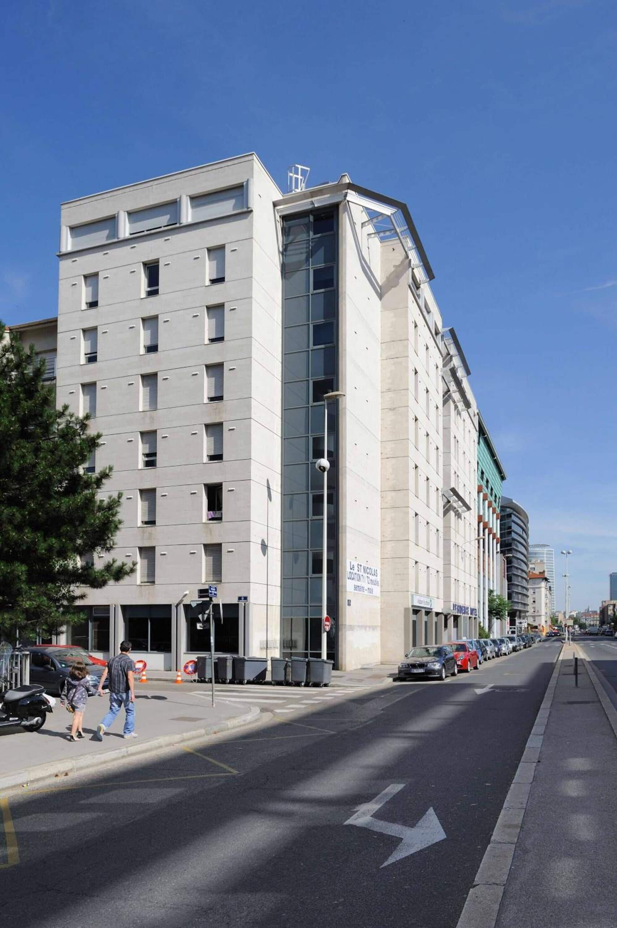 A multi-story building with a modern architectural design, featuring a prominent corner entrance and a visible sign indicating it is a hotel.