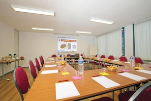 A conference room with a long table, red chairs, and a projector screen displaying a presentation.