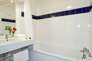 A bathroom with a white sink, mirror, and bathtub. There is a towel rack and a shower curtain. - Séjours & Affaires Lyon Saint-Nicolas (Lyon)