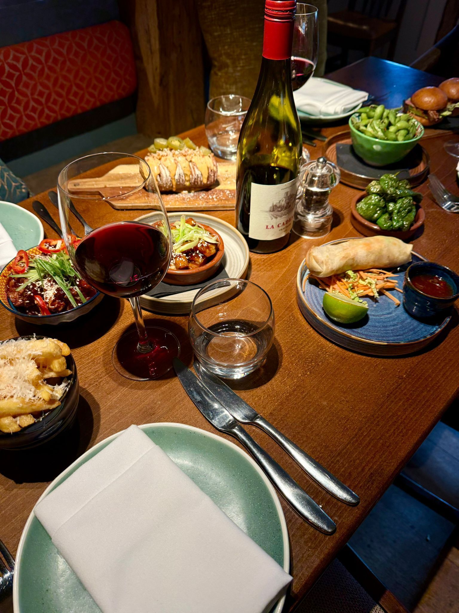 Une table à manger avec différents plats, une bouteille de vin et des couverts.