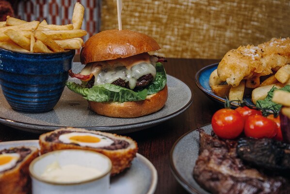 Een maaltijd bestaande uit een hamburger, friet, fish and chips en een steak, met saus erbij.