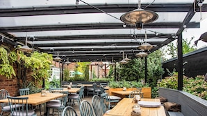 An outdoor patio with wooden tables and chairs, covered by a pergola with hanging lights. - The Winning Post (Windsor)