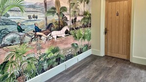 A hallway with a mural depicting a tropical landscape, a wooden door, and a light fixture. - The Winning Post (Windsor)