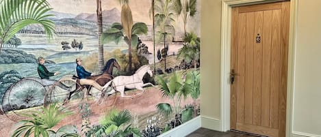 A hallway with a mural depicting a tropical landscape, a wooden door, and a light fixture.