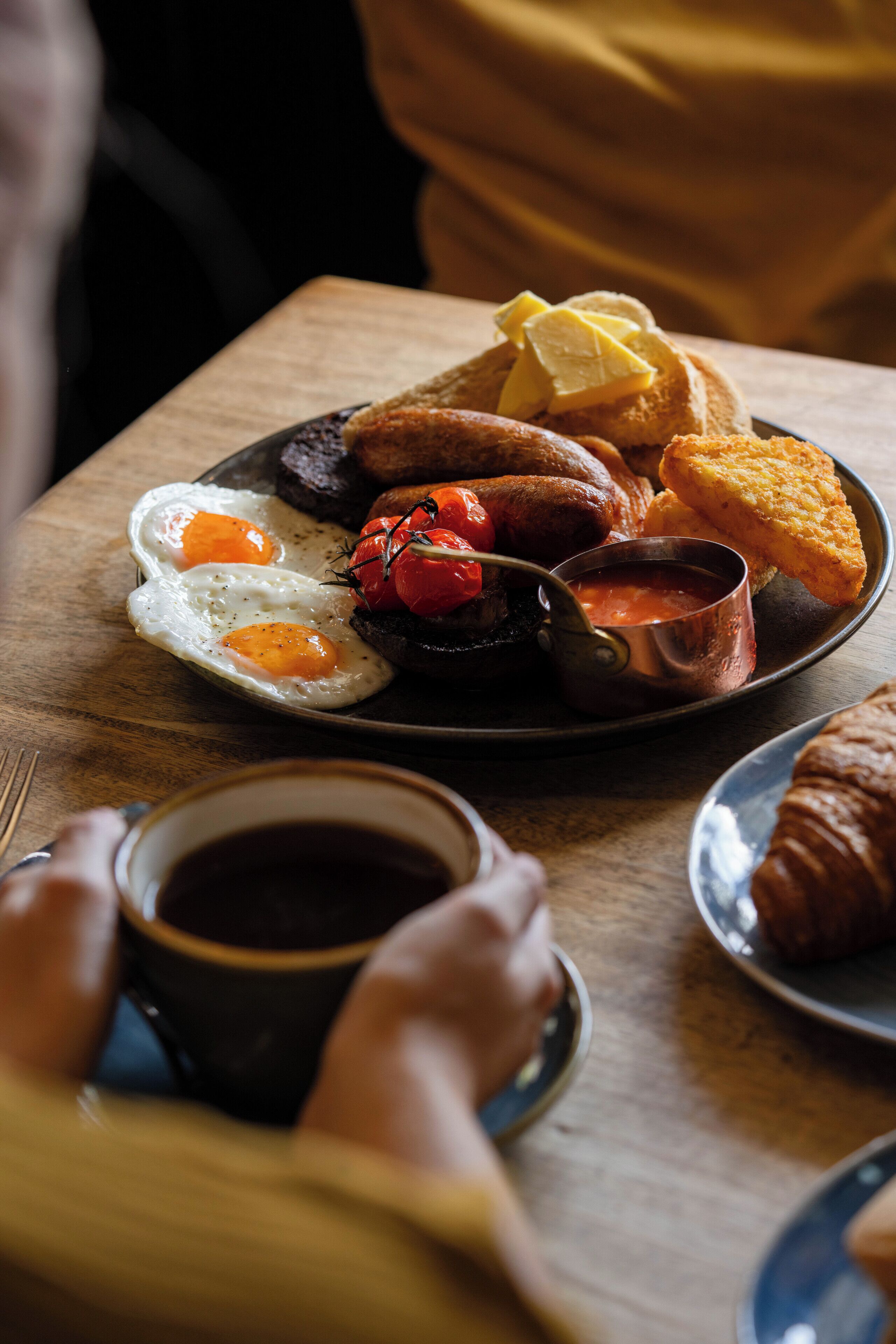 A breakfast plate with eggs, sausages, toast, and a cup of coffee on a wooden table.