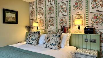 A bedroom with a bed, two pillows, a nightstand, a lamp, a radio, and a framed picture on the wall.