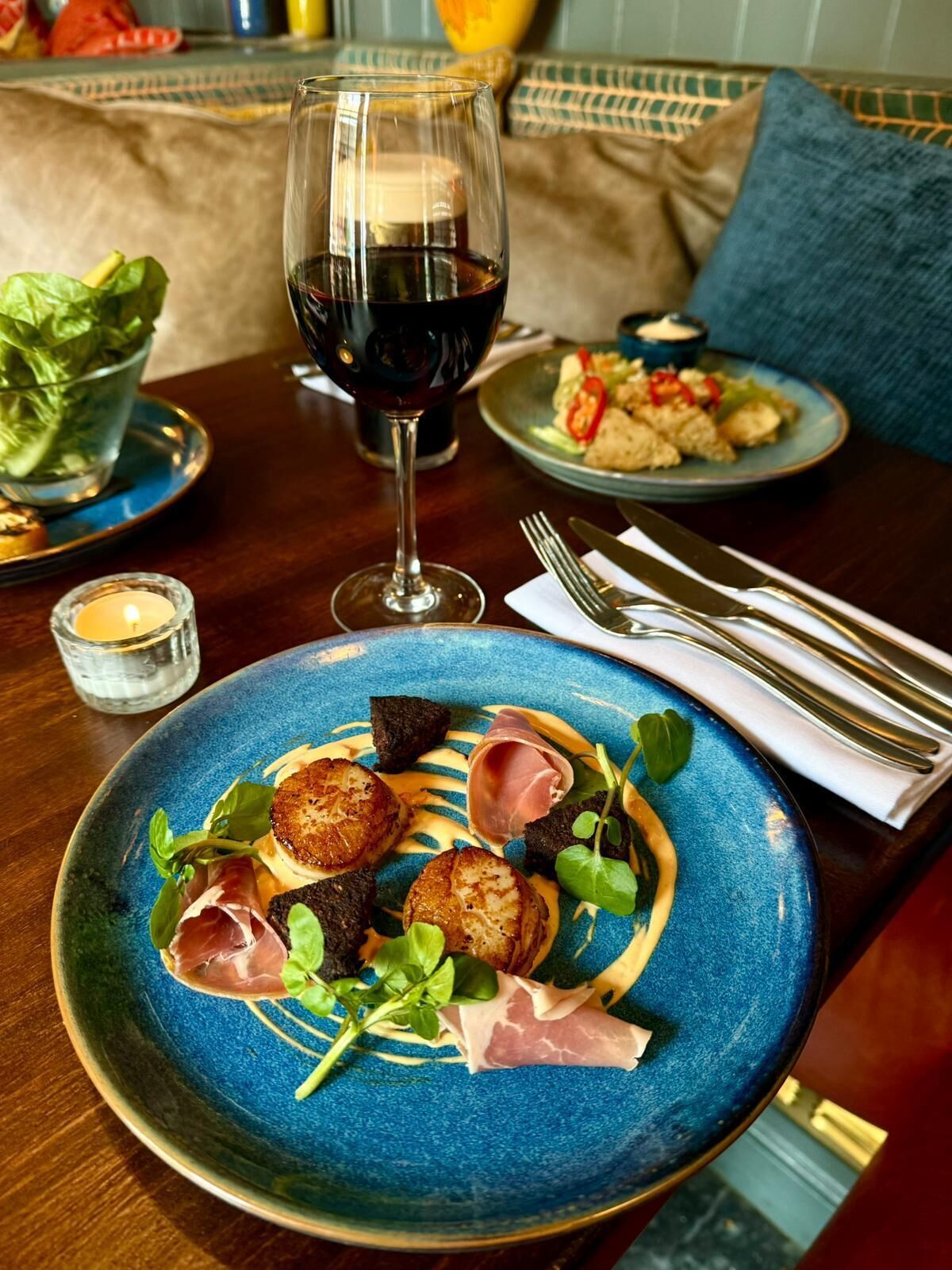 Una mesa de comedor con un plato de comida azul, una copa de vino tinto y una vela.