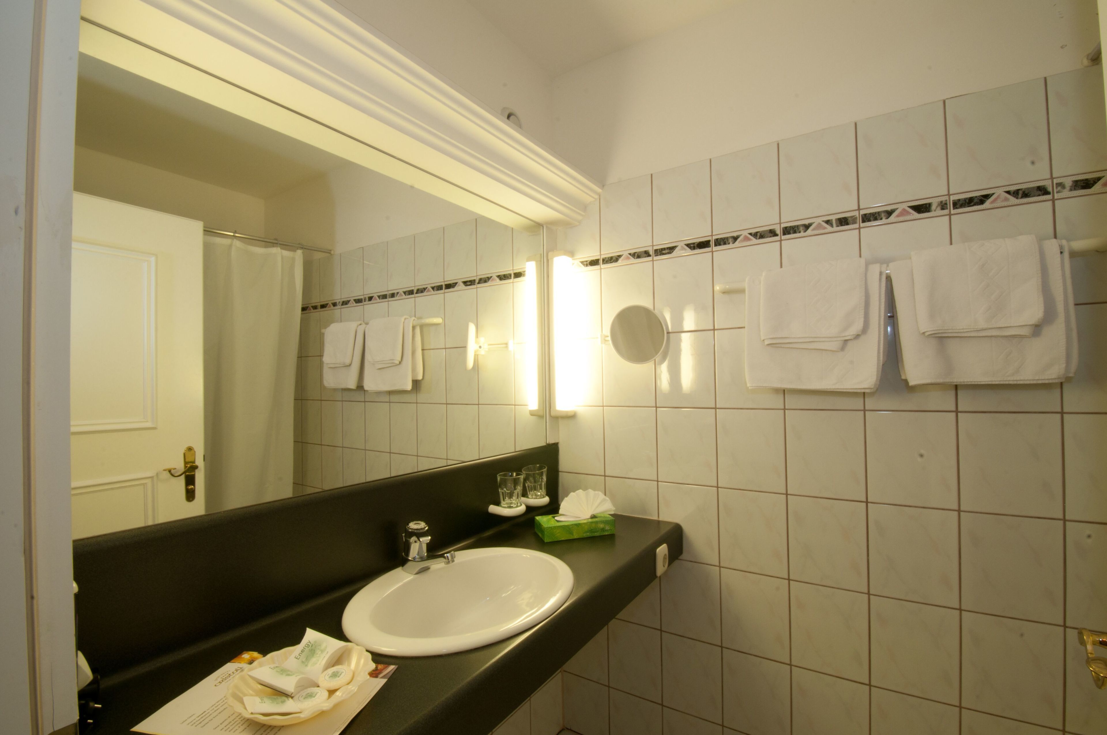 Un baño con lavamanos blanco, espejo y toallero con varias toallas.